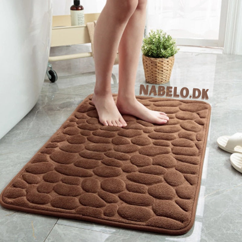 Textured cobblestone bath mat with rounded corners on a bathroom floor