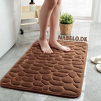 Textured cobblestone bath mat with rounded corners on a bathroom floor