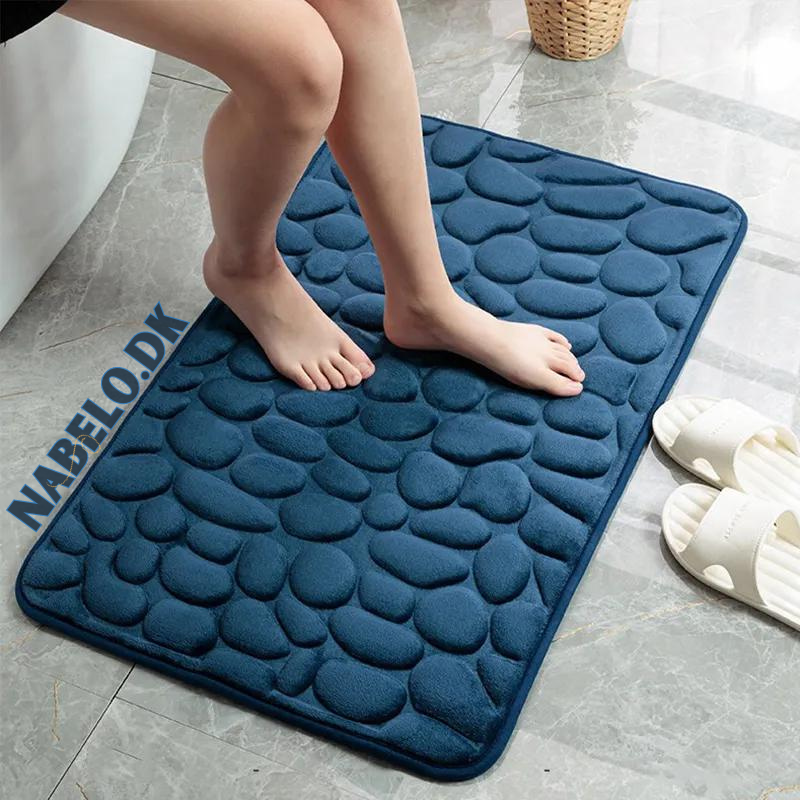 Textured cobblestone bath mat with rounded corners on a bathroom floor