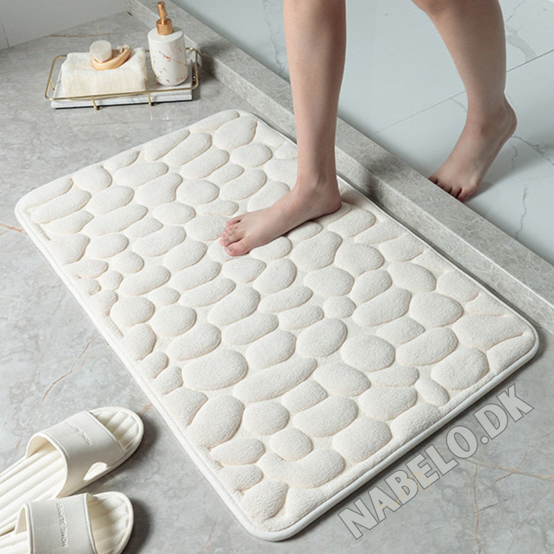 Textured cobblestone bath mat with rounded corners on a bathroom floor