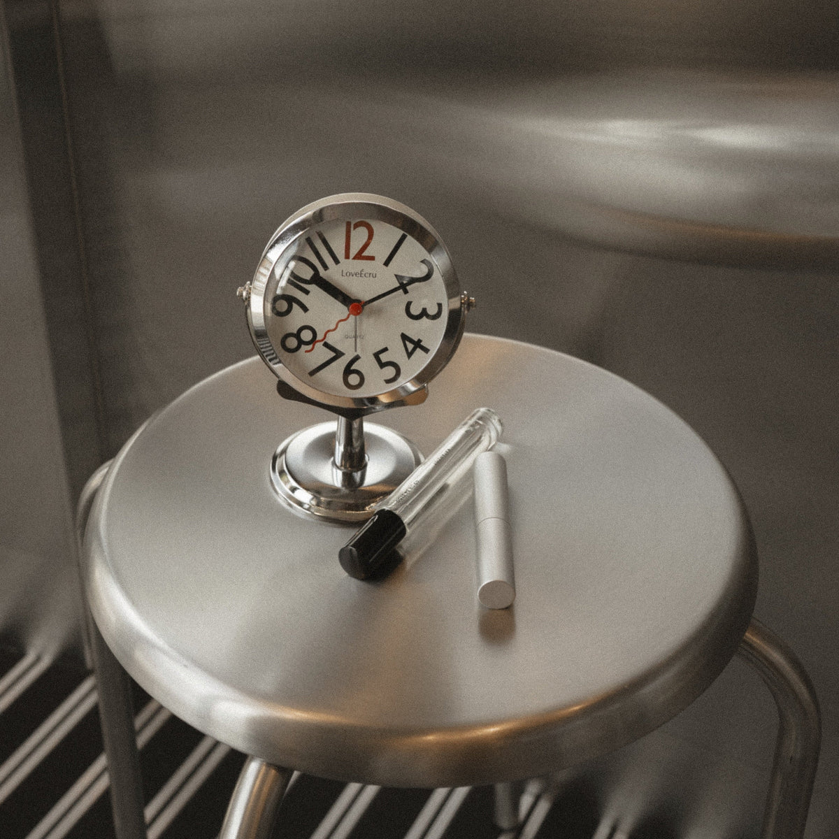 Round analogue alarm clock with bold numerals and raised metallic-effect stand