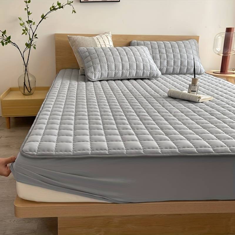 Quilted mattress protector with a padded square design on a bed